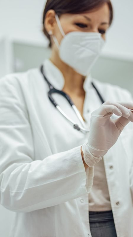 Medical exam. Doctor using tongue depressor and wearing protective face mask.