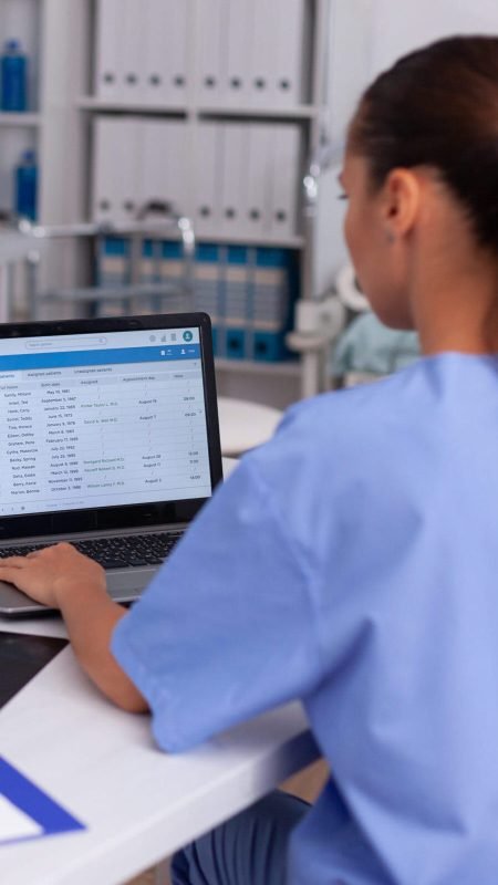 Medical nurse checking patient documentation on laptop in hospital office. Health care physician using computer in modern clinic looking at monitor, medicine, profession, scrubs.